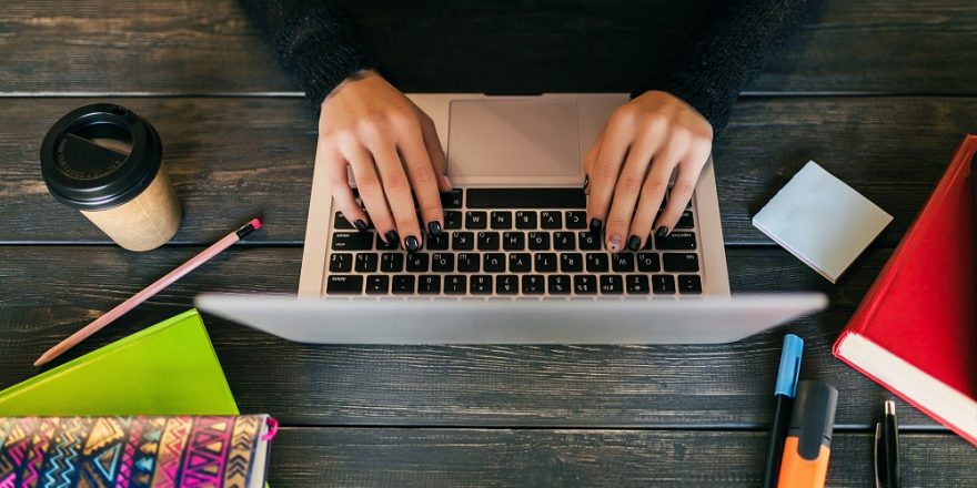 view from above on hands of pretty woman sitting at table in black shirt working on laptop in co-working office, stationery, hands typing, drinking coffee, freelance